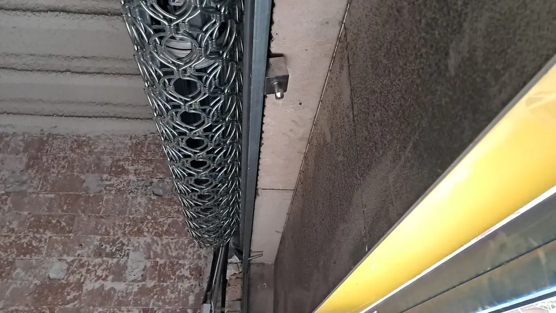Cierre de ballesta recogido, visto desde abajo junto al toldo amarillo de un local